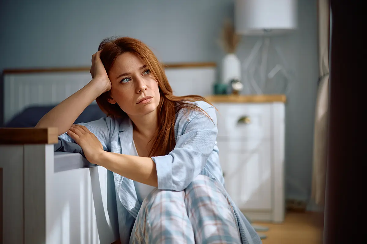 Depressed woman sitting floor bedroom morning