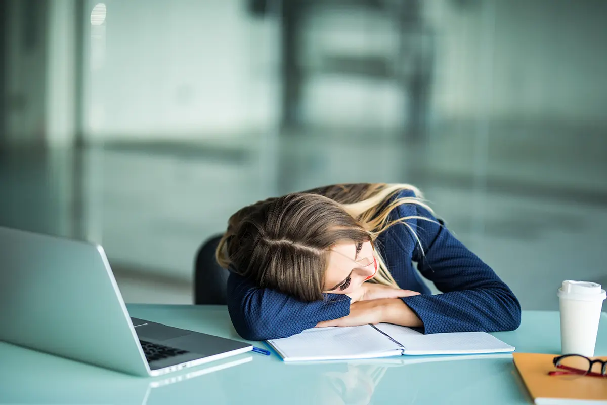Pretty exhausted young businesswoman sitting her desk sleeping her office